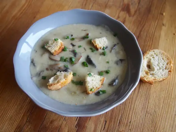 Un réconfortant velouté de champignon, garni de croûtons dorés et de ciboulette fraîche, servi dans un bol bleu sur une table en bois.